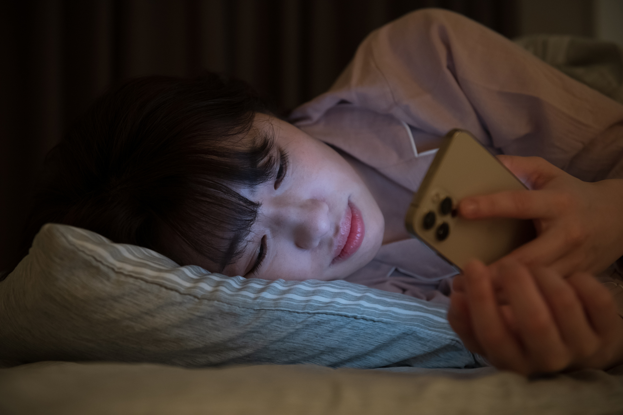 暗がりのベッドでスマートフォンを見ている女性