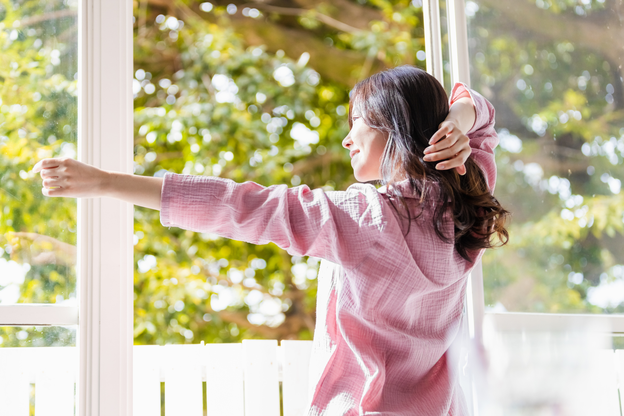 窓を開けて太陽光を浴びる女性