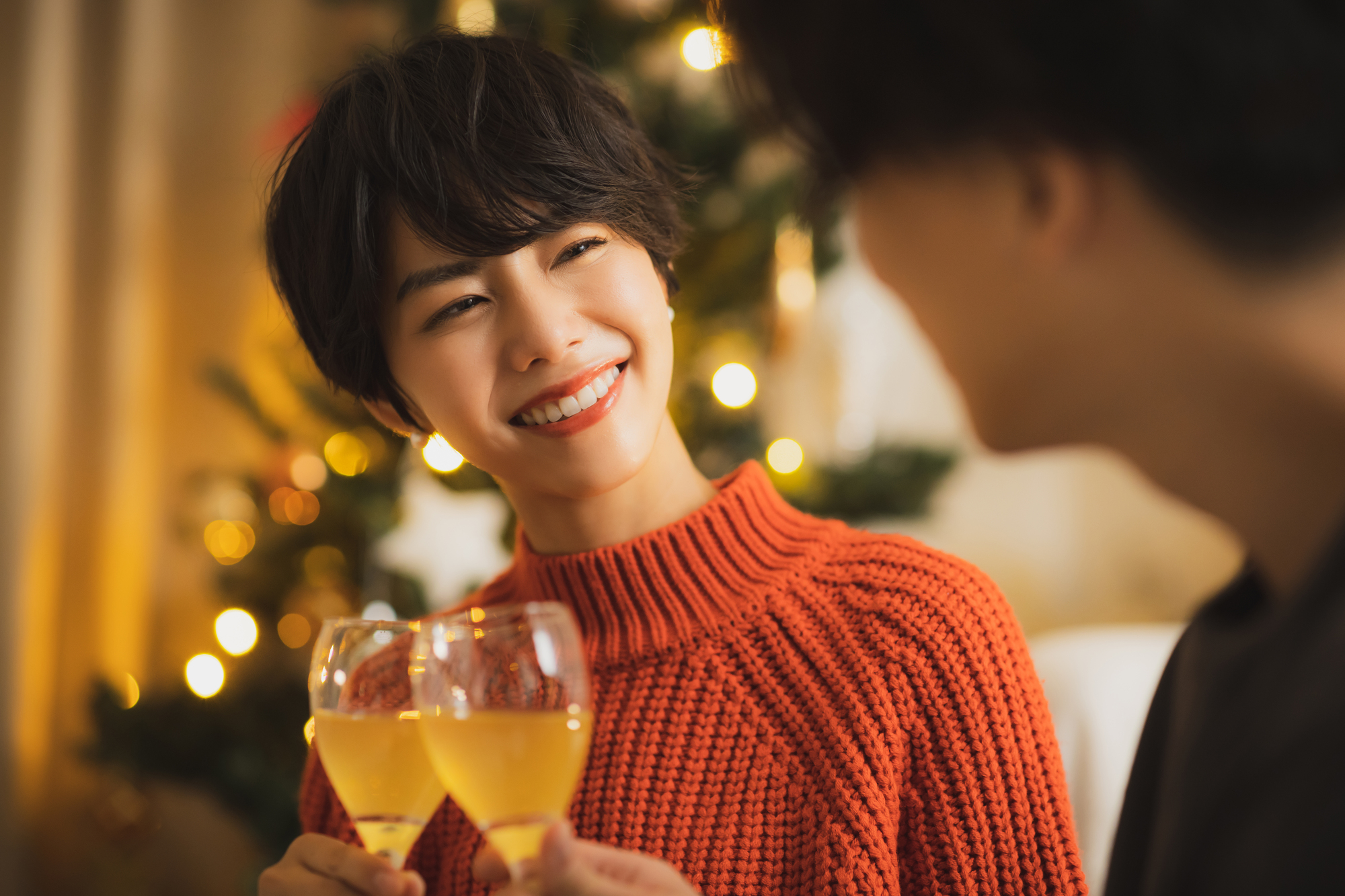 クリスマスツリーの前、シャンパングラスで乾杯する男女の様子