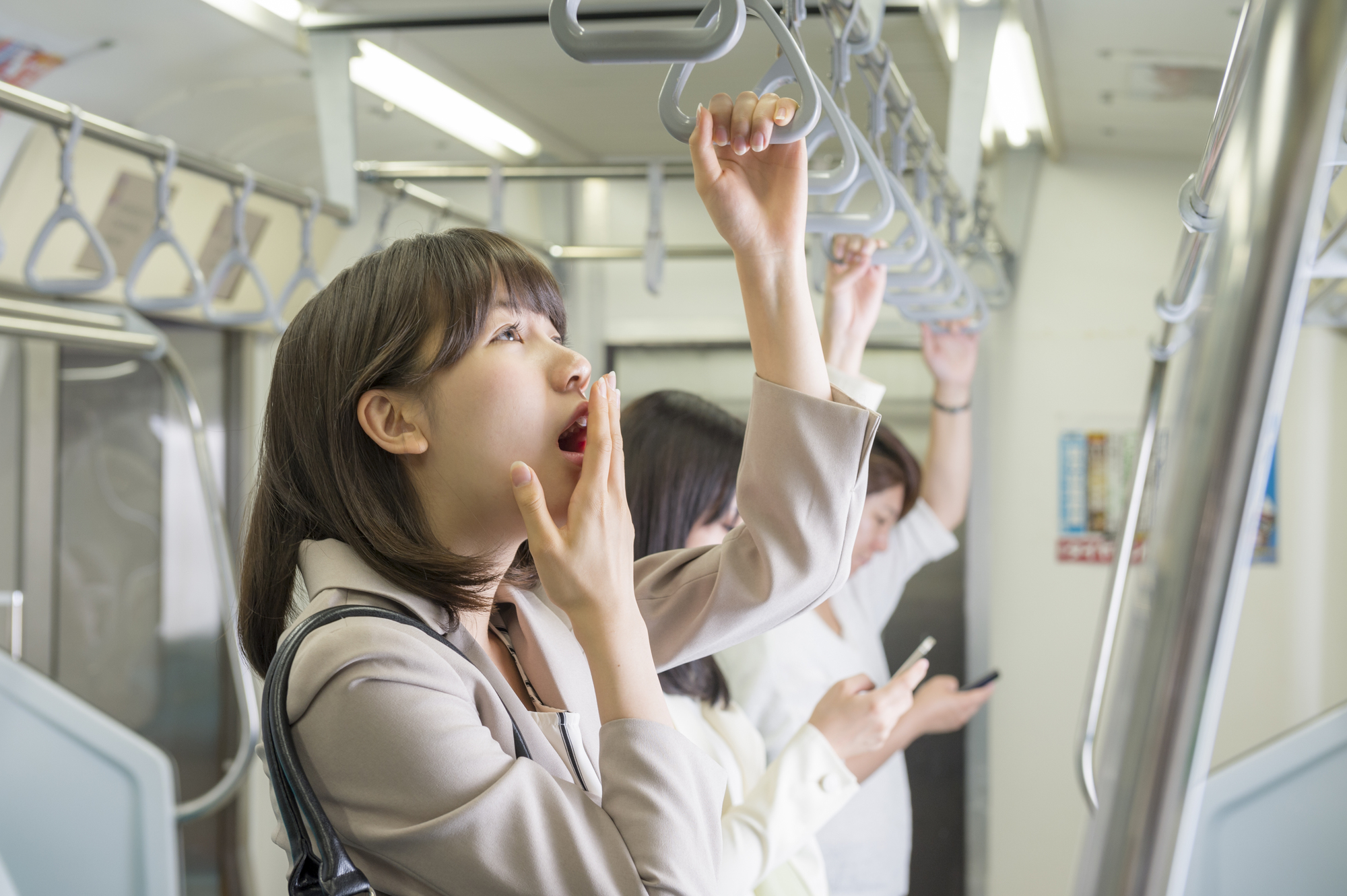 あくびをしながら電車通勤する女性