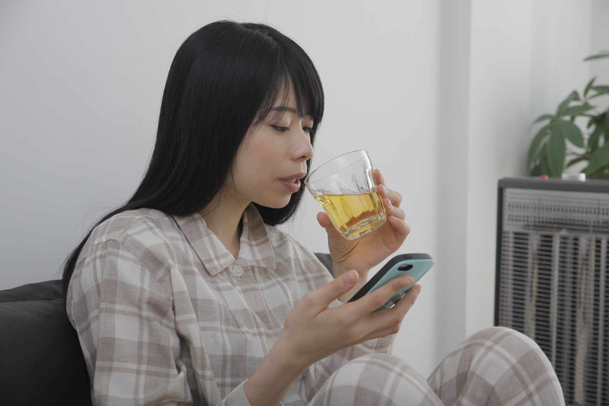 スマホをいじりながら飲み物を飲む女性