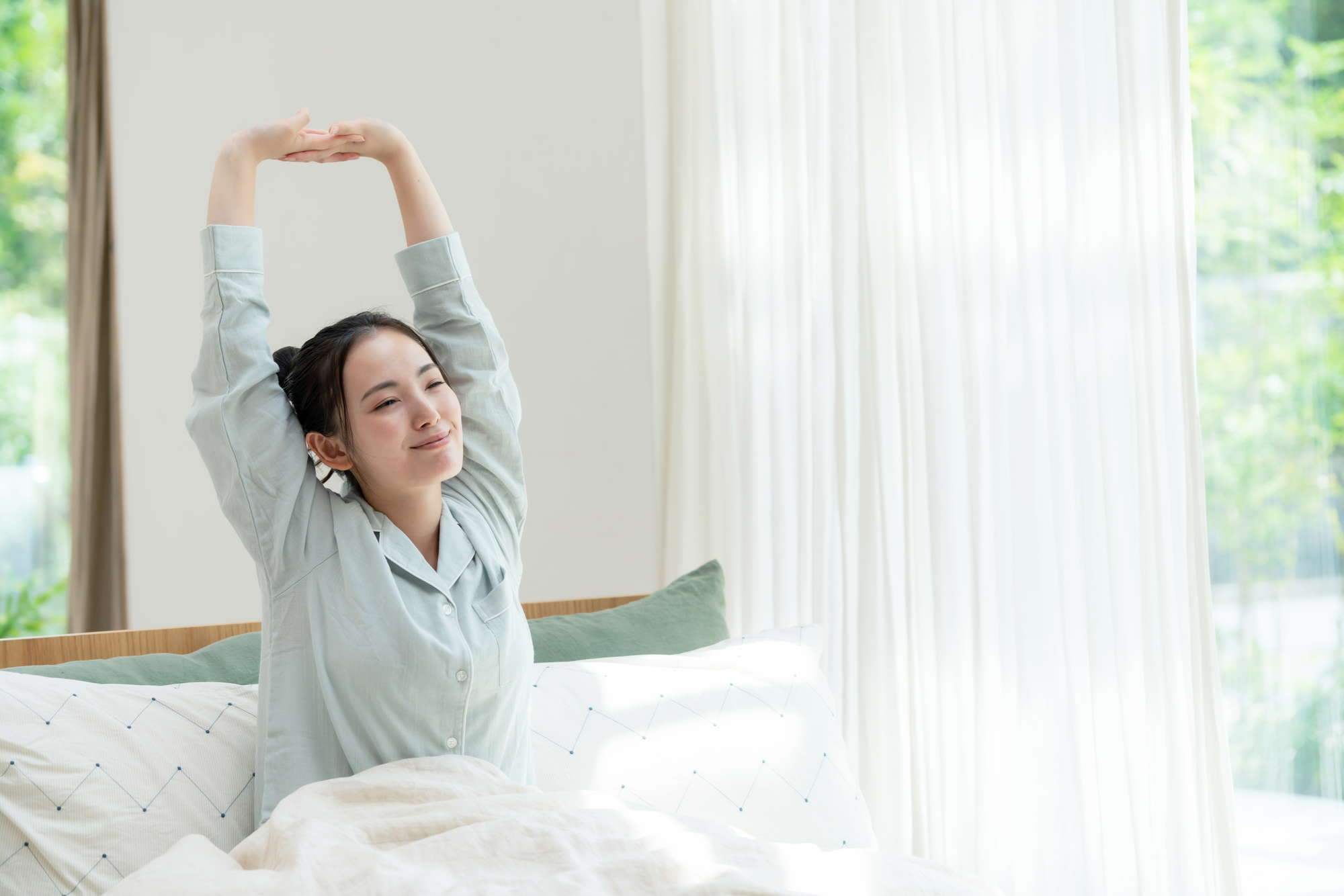 ベッドで伸びをする寝起きの女性